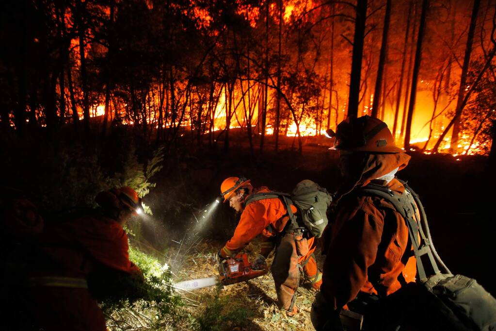Inmate Jose Jimenez, center, of Cal Fire Mt. Bullion Crew 2, cuts down roadside vegetation with his chainsaw while other inmate crewmembers pull the loose brush away, at the Oakmont fire off Highway 12 in Santa Rosa, California on Tuesday, October 17, 2017. (Alvin Jornada / The Press Democrat)