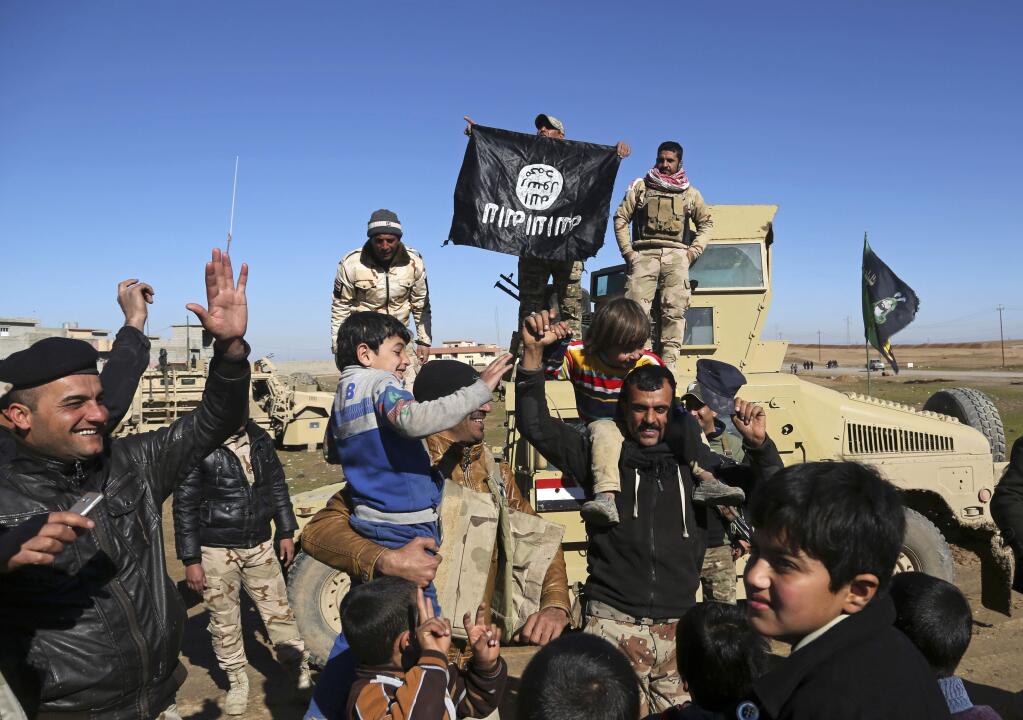 Iraqi Army soldiers celebrate with residents of liberated neighborhoods as they hold upside down a flag of the Islamic State group, in the eastern side of Mosul, Iraq, Tuesday, Jan. 24, 2017. The U.N. and several aid organizations say an estimated 750,000 civilians are still living under Islamic State rule in Mosul despite recent advances by Iraqi forces. Lise Grande, the U.N. Humanitarian Coordinator for Iraq, said in a statement Tuesday that the cost of food and basic goods is soaring, water and electricity are intermittent and that some residents are forced to burn furniture to keep warm. (AP Photo/Khalid Mohammed)
