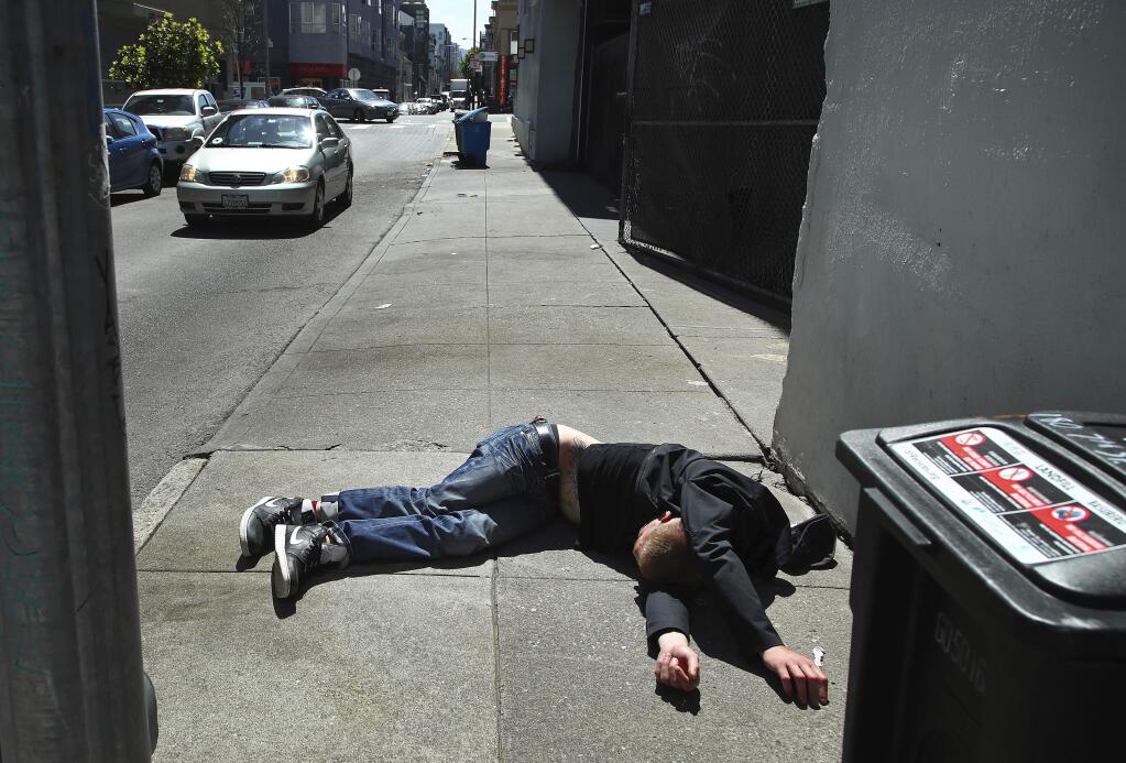 FILE - In this April 26, 2018, file photo, a man lies on the sidewalk beside a recyclable trash bin in San Francisco. San Francisco voters will decide in November 2018 whether to tax large businesses to pay for homeless and housing services in a city struggling with income inequality. Supporters collected enough signatures to get the measure on the ballot. (AP Photo/Ben Margot, File)