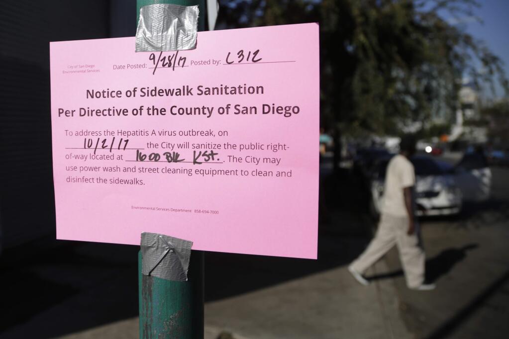 A man passes behind a sign warning of an upcoming street cleaning along 17th Street on Thursday, Sept. 28, 2017, in San Diego. The city of San Diego has cleared a downtown street where hundreds of homeless people regularly camp during ongoing efforts to sanitize neighborhoods to control the spread of hepatitis A. (AP Photo/Gregory Bull)
