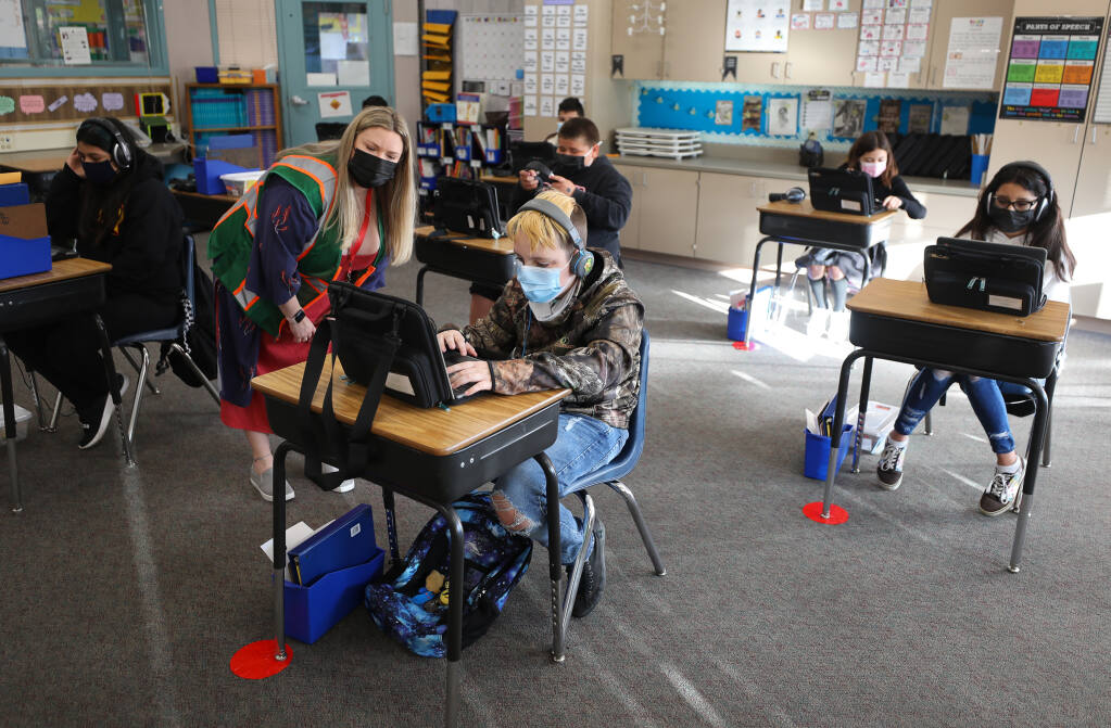 Fifth-grade teacher Alissa Esposito keeps her distance while helping Skyler Koppenhaver log in on his computer at Brook Hill Elementary School in Santa Rosa on Thursday, April 1, 2021.  (Christopher Chung/ The Press Democrat)