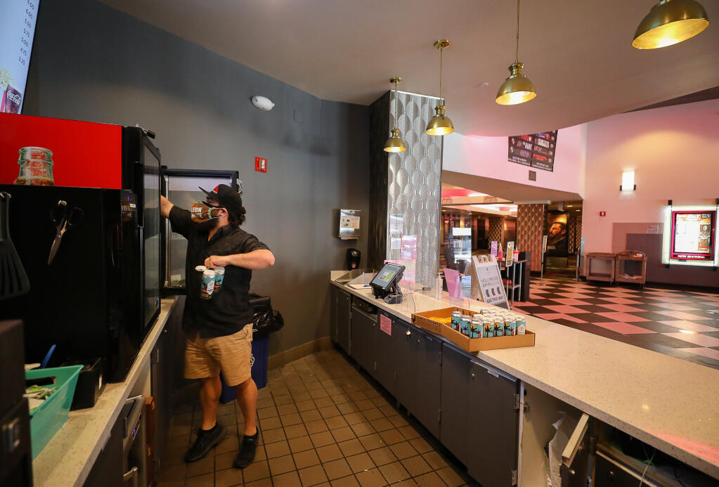 Scott Timko restocks a refrigerator at the concession stand in the Roxy Stadium 14 movie theater in Santa Rosa on Monday, March 29, 2021.  The movie theater will reopen on Wednesday, March 31.  (Christopher Chung / The Press Democrat)