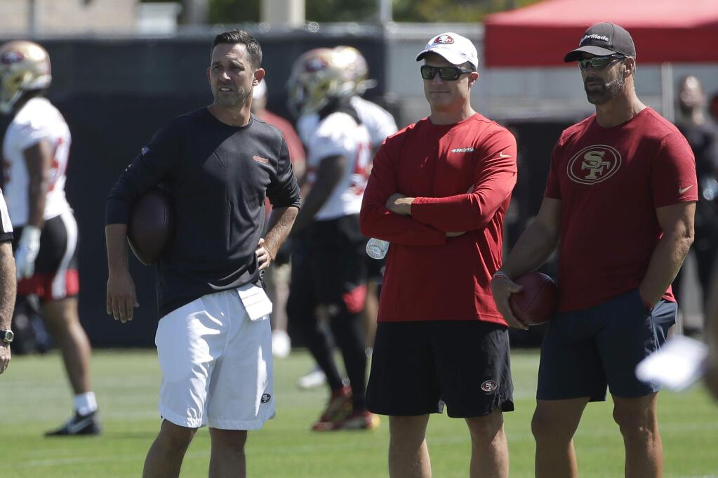 San Francisco 49ers head coach Kyle Shanahan, from left, watches as players practice, with general manager John Lynch and broadcaster Tim Ryan, right, at training camp in Santa Clara, Saturday, July 27, 2019. (AP Photo/Jeff Chiu)