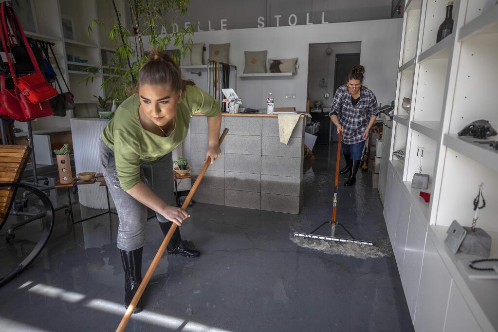Valentina Stoll helps her mom Adelle squeegee water from her business, Adelle Stoll, in the Barlow business district in Sebastopol on Thursday. (John Burgess/The Press Democrat)