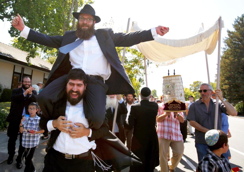 Rabbai Mendel Wolvovsky, upper left, is carried on the shoulders of Rabbi Raleigh Resnick of Pleasanton as they dance ahead of the Torah in a celebratory procession marking the completion of the handwritten Torah at the Joseph Weingarten Chabad Jewish Center in Santa Rosa, California, on Sunday, August 27, 2017. (Alvin Jornada / The Press Democrat)