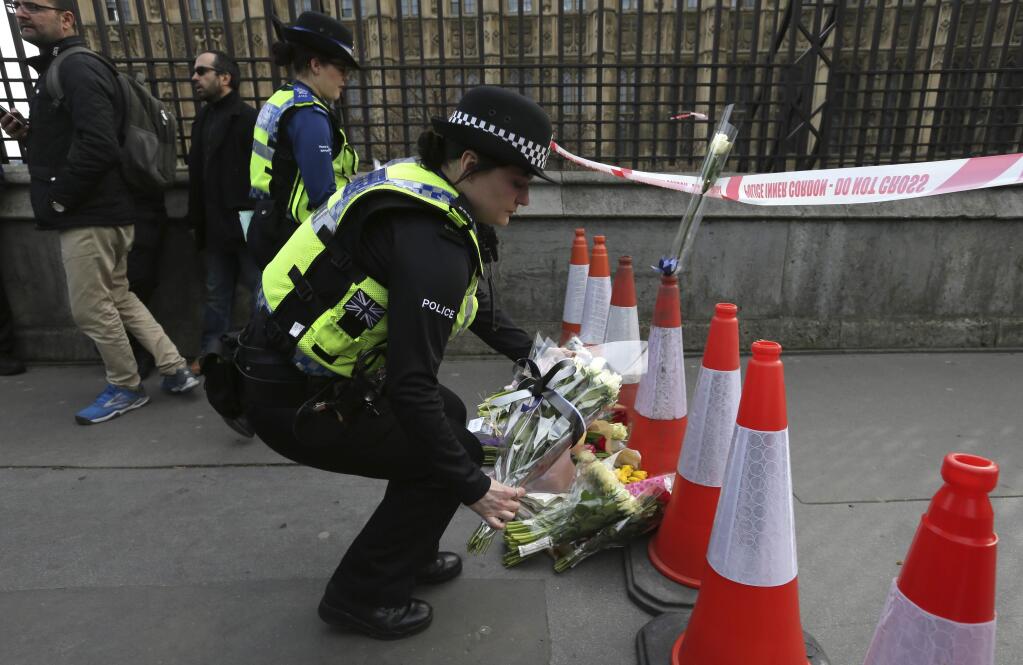 Police officers lays flowers as part of a floral tribute to the victims of Wednesday's attack placed near the Houses of Parliament in London, Thursday March 23, 2017. On Wednesday a knife-wielding man went on a deadly rampage, first driving a car into pedestrians then stabbing a police officer to death before being fatally shot by police within Parliament's grounds in London. (AP Photo/Tim Ireland)