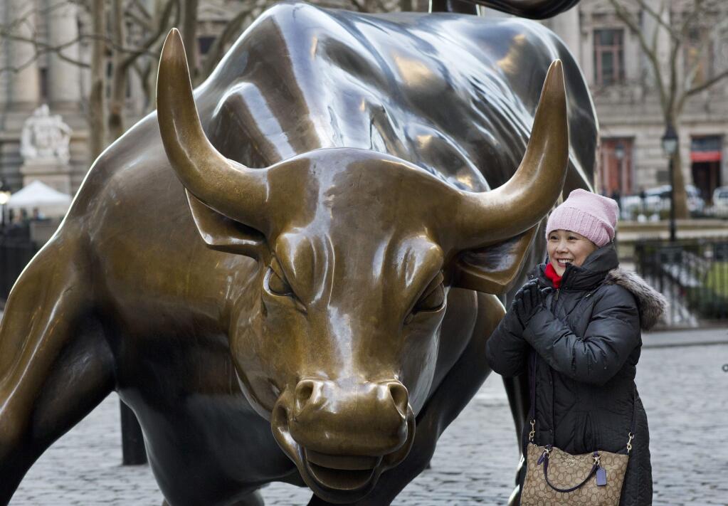 In this March 23, 2017 photo, a woman poses for photos with the Charging Bull statue in New York. Since 1989 the massive, bronze bull has stood in New York City's financial district as an image of the might and hard-charging spirit of Wall Street. (AP Photo/Mark Lennihan)
