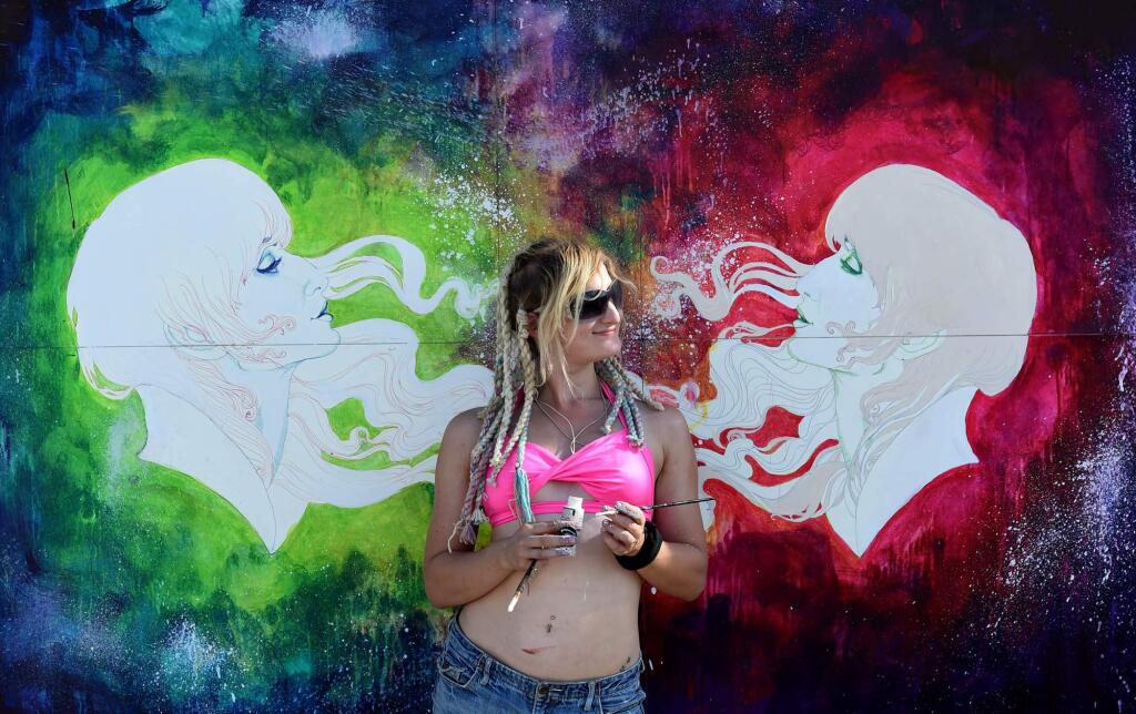 In this Aug. 25, 2014 photo, a woman poses in front of a paining during Burning Man in the Black Rock Desert of Gerlach, Nev. Organizers call Burning Man the largest outdoor arts festival in North America, with its drum circles, decorated art cars, guerrilla theatrics and colorful theme camps. (AP Photo/The Reno Gazette-Journal, Andy Barron)
