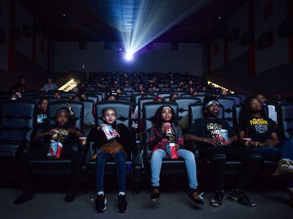 Mari Copeny, third from left, watches a free screening of the film 'Black Panther' with more than 150 children, after she raised $16,000 to provide free tickets in an entire theater on Monday, Feb. 19, 2018 in Flint Township, Mich. As 'Black Panther' debuts in theaters across the U.S., educators, philanthropist, celebrities and business owners are pulling together their resources to bring children of color to see the film that features a black superhero in a fictional, un-colonized African nation. (Jake May /The Flint Journal-MLive.com via AP)