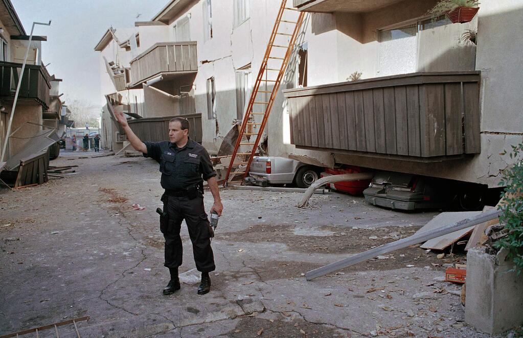 FILE - In this Jan. 17, 1994 file photo, a Los Angeles police officer stands in front of the Northridge Meadows Apartment building, after the upper floors of the structure collapsed onto the open garages and first story, killing 16 people in Los Angeles. A report Tuesday, March 10, 2015, by the U.S. Geological Survey found that the odds of a magnitude-6.7 quake similar in size to the 1994 Northridge disaster was higher in Northern California than Southern California 95 percent versus 93 percent. (AP Photo/Chuck Jackson, File)