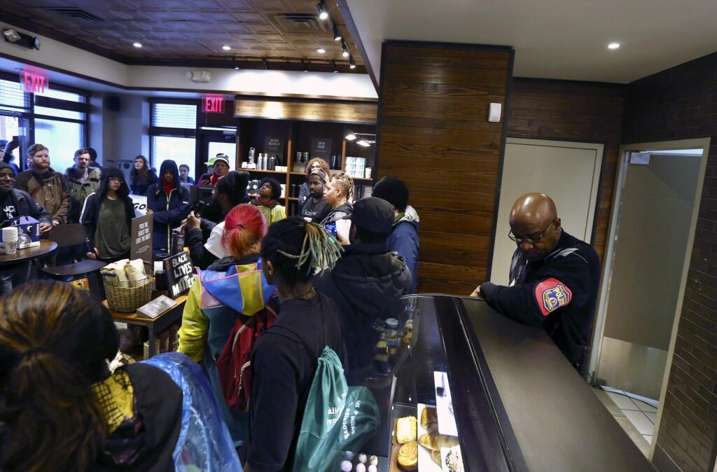 A plain-clothed police officer, right, mans a position behind the counter at the Starbucks that has become the center of protests Monday, April 16, 2018, in Philadelphia. The CEO of Starbucks arrived in Philadelphia hoping to meet with two black men who were arrested when the coffee chain's employees called 911 and said they were trespassing. Meanwhile, protesters took over the shop Monday. (AP Photo/Jacqueline Larma)