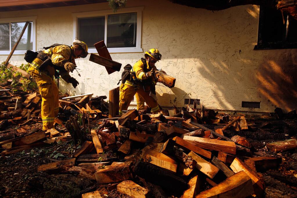 San Jose firefighters clear firewood away from a house on Deer Park Drive after the Tubbs fire burned through north Santa Rosa, California on Monday, Oct. 9, 2017. (ALVIN JORNADA/ PD FILE)