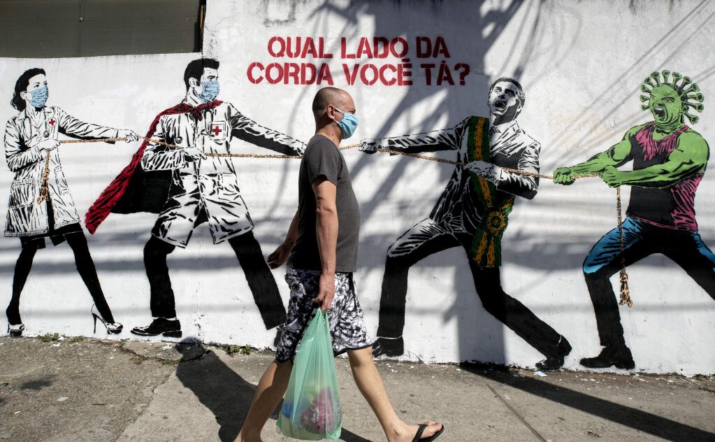 A man, wearing a protective face mask as a measure to curb the spread of the new coronavirus, walks past a mural depicting a tug-of-war between health workers and Brazil's President Jair Bolsonaro aided by a cartoon-styled coronavirus character, with a message that reads in Portuguese: 'Which side are you on?,' in Sao Paulo, Brazil, Friday, June 19, 2020. (AP Photo/Andre Penner)