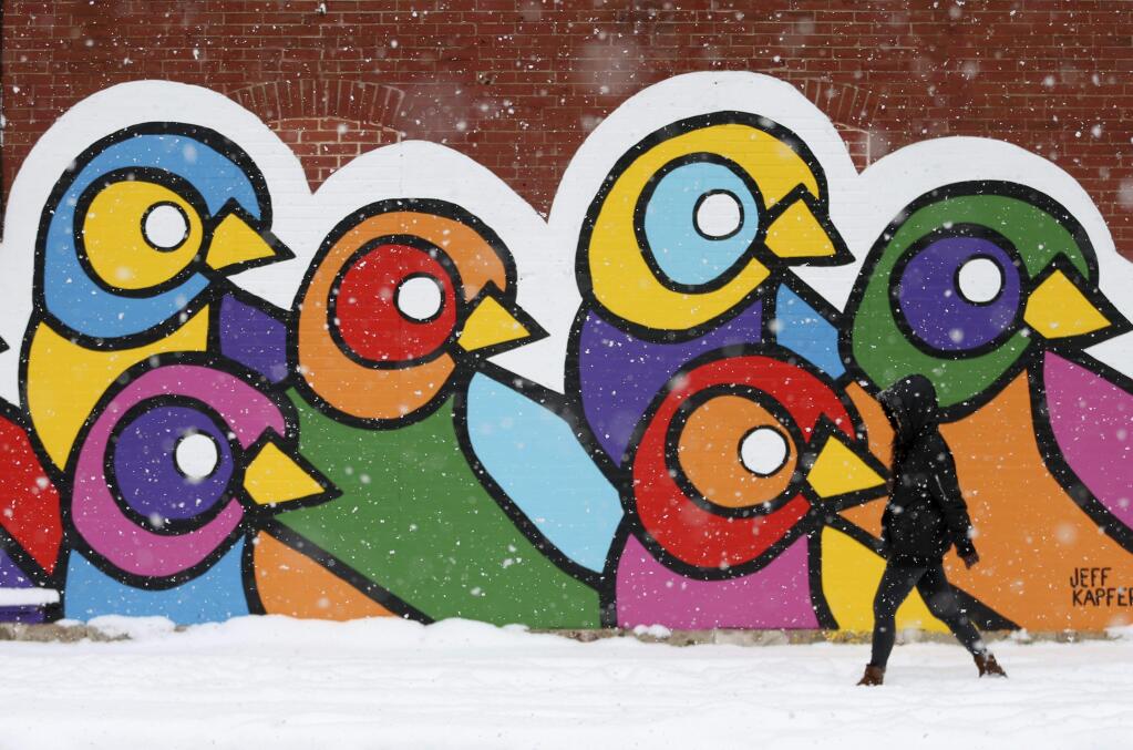 'The snow is just beautiful, ' said Xioqing Qin, who walks to work in the snow passing a mural painted on the exterior wall of the Atomic Cowboy bar and restaurant on Thursday, Nov. 15, 2018, in St. Louis. (Laurie Skrivan, lskrivan/St. Louis Post-Dispatch via AP)