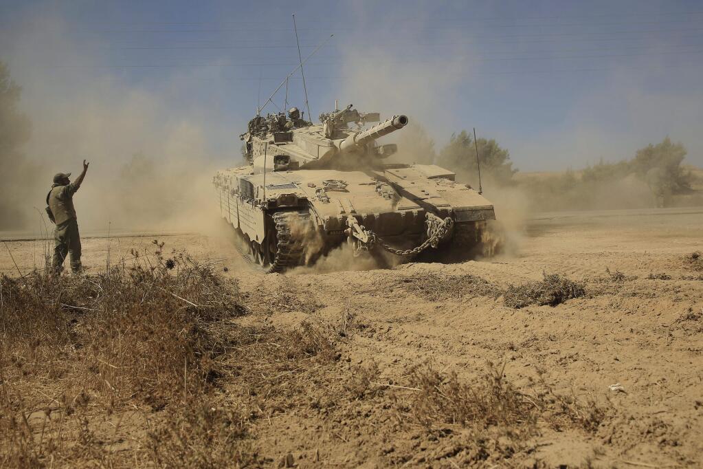 Israeli reserved soldiers direct a Merkava tank to cross a road in the southern Israel as it advances towards the Israel Gaza border, Friday, Aug. 1, 2014. (AP Photo/Tsafrir Abayov)