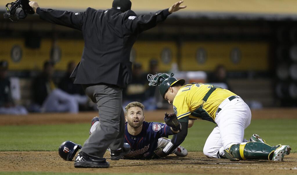 The Minnesota Twins' Brian Dozier looks to home plate umpire Mark Ripperger for the call as he scores past Oakland Athletics catcher Ryan Lavarnway, right, during the fourth inning Friday, July 28, 2017, in Oakland. (AP Photo/Ben Margot)