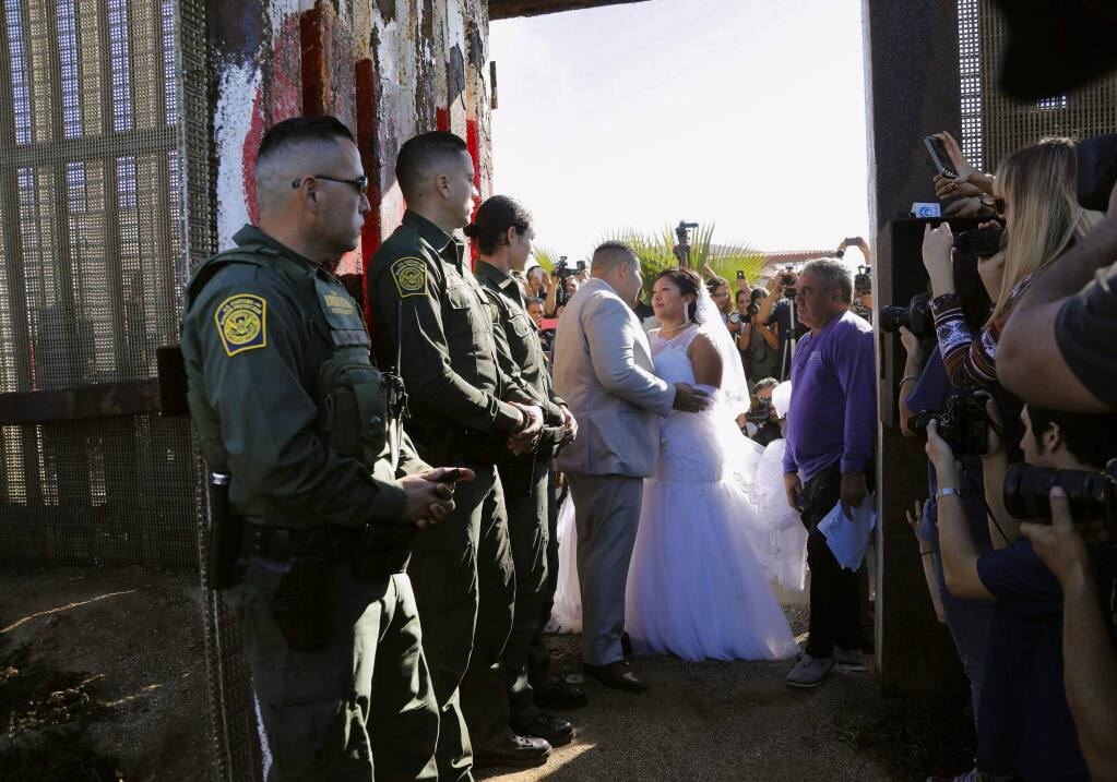 In this Nov. 18, 2017, photo, Brian Houston, of Rancho San Diego, center left, and Evelia Reyes, right, of Tijuana, Mexico, look at each other in their wedding at the 'Door of Hope,' part of the border fence between the U.S. and Mexico. A U.S. citizen, forbidden to enter Mexico, met and wed the love of his life in a brief moment when the gate separating the two countries was opened. Now it turns out the groom is a convicted drug smuggler and border agents are furious that he passed a federal background check and was approved for the 'Door of Hope.' (Howard Lipin//The San Diego Union-Tribune via AP)