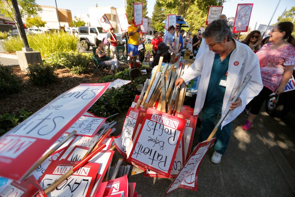 Orthopedic lab technician Art Hernandez, who was recently laid off from Santa Rosa Memorial Hospital, picks out a sign to carry as other hospital employees and their supporters protest against more potential layoffs at the hospital, in Santa Rosa, California, on Friday, June 29, 2018. (Alvin Jornada / The Press Democrat)