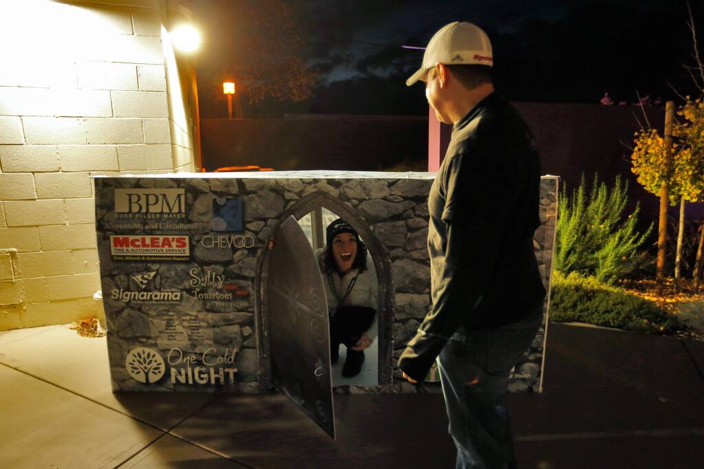 Social Advocates for Youth Cat Cvengros, left, tries out a cardboard box made by participant Aaron Friedman, right, owner of Sign-a-rama, featuring logos of businesses that sponsored him for Social Advocates for Youth's One Cold Night event at the SAY Dreamcenter in Santa Rosa, California on Friday, November 18, 2016. (Alvin Jornada / The Press Democrat)