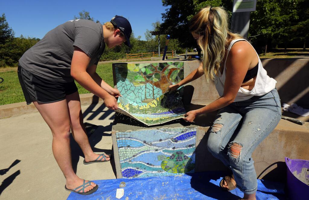ArtStart apprentice Matti Hathaway, left, and project manager Angelina Duckett install mosaic panels on a bench at the Children's Memorial Grove at Spring Lake Regional Park. (JOHN BURGESS/ PD)
