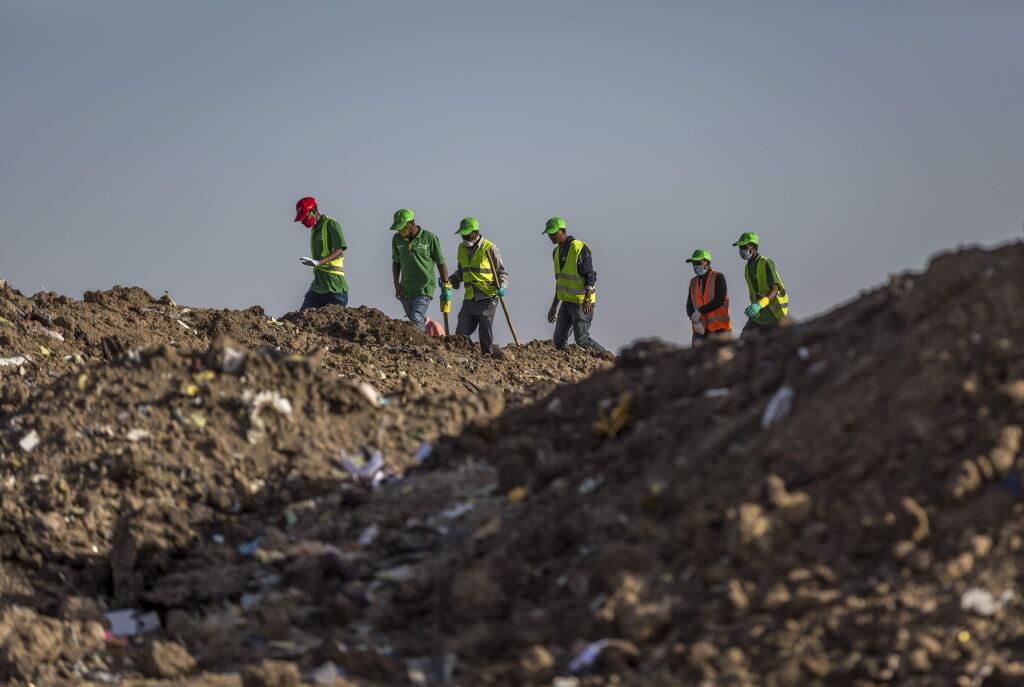 Workers walk to collect clothes and other materials, under the instruction of investigators, at the scene where the Ethiopian Airlines Boeing 737 Max 8 crashed shortly after takeoff on Sunday killing all 157 on board, near Bishoftu, or Debre Zeit, south of Addis Ababa, in Ethiopia Tuesday, March 12, 2019. Ethiopian Airlines had issued no new updates on the crash as of late afternoon Tuesday as families around the world waited for answers, while a global team of investigators began picking through the rural crash site. (AP Photo/Mulugeta Ayene)