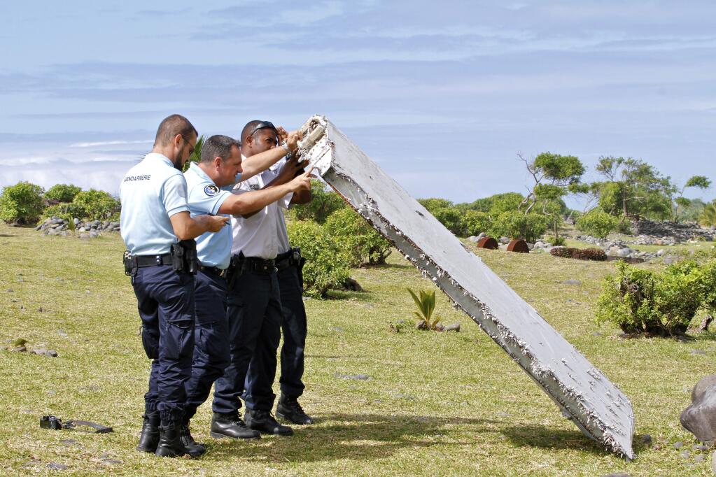 FILE - In this July 29, 2015 file photo, French police officers inspect a piece of debris from a plane in Saint-Andre, Reunion Island. Confirmation that a wing flap found on an island in the western Indian Ocean is part of Malaysia Airlines Flight 370 would add a critical piece to the puzzle of the Boeing 777s disappearance 17 months ago. Malaysian Prime Minister Najib Razak delivered that confirmation Thursday, Aug. 6, 2015 though French, U.S. and Australian investigators stopped just short of that, saying the part is from a 777 and acknowledging that Flight 370 is the only 777 missing. Examination of the part is continuing. (AP Photo/Lucas Marie, File)