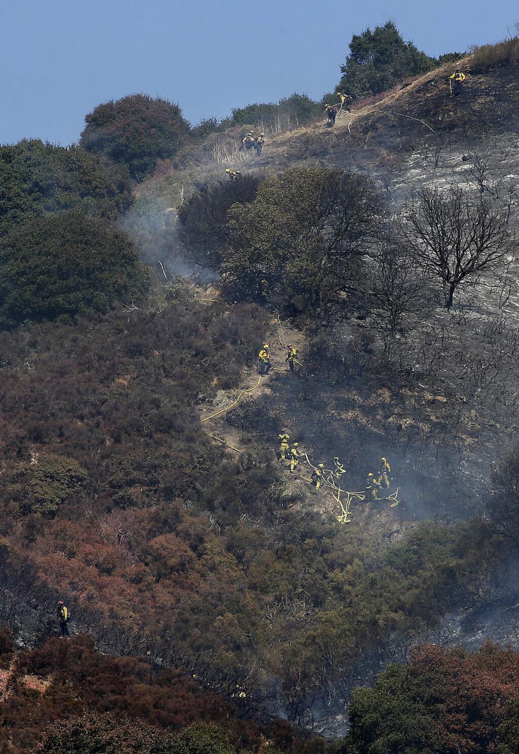 A crew of firefighters work along the Oakland Hills in Oakland, Calif., Tuesday, Sept. 26, 2017. Officials in Oakland say residents were being evacuated from an area near a fast-moving grass fire that was threatening at least 50 structures including several homes. (AP Photo/Jeff Chiu)