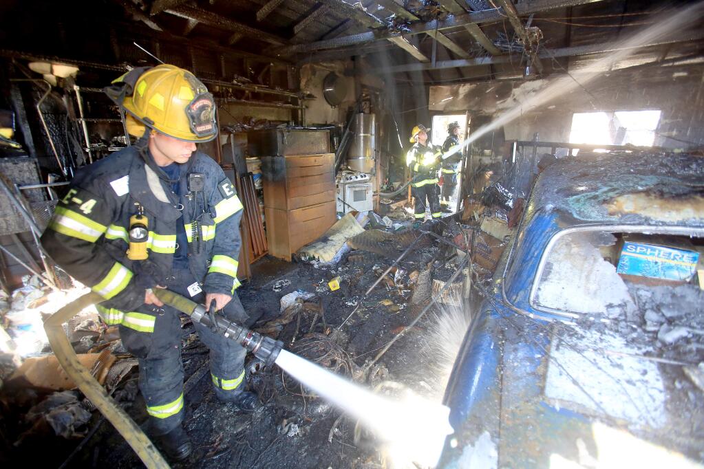 Santa Rosa firefighters spray water in a garage onto a burned car along Corby Avenue after power lines caused a grass fire which spread into the home Monday July 27, 2015 in Santa Rosa. (Kent Porter / Press Democrat)