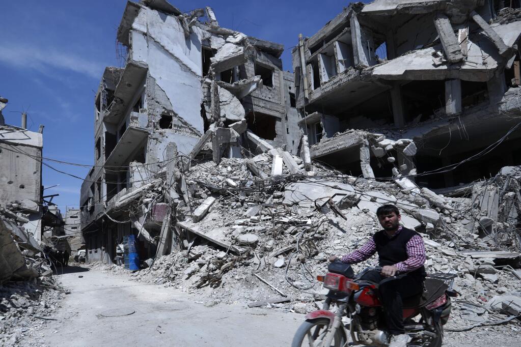 A man rides past destruction in the town of Douma, the site of a suspected chemical weapons attack, near Damascus, Syria, Monday, April 16, 2018. Faisal Mekdad, Syria's deputy foreign minister, said on Monday that his country is 'fully ready' to cooperate with the fact-finding mission from the Organization for the Prohibition of Chemical Weapons that's in Syria to investigate the alleged chemical attack that triggered U.S.-led airstrikes. (AP Photo/Hassan Ammar)