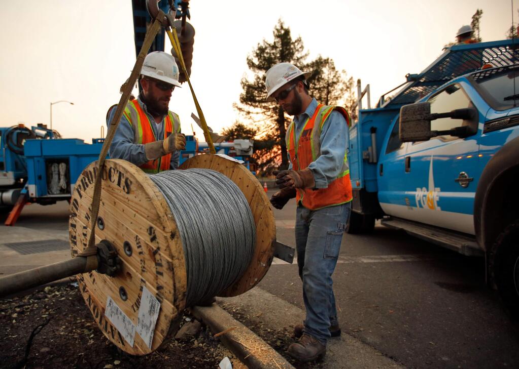 PG&E workers Gary Callinan, left, and Terry Lane hoist a 2,500-foot spool of guy wire to be used to provide backup tension to the power line their crews will string across Highway 101 in Santa Rosa, California on Wednesday, Oct. 11, 2017. (Alvin Jornada / The Press Democrat)