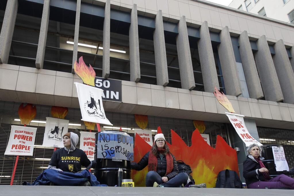 Protesters sit outside of an entrance to a Pacific Gas & Electric building in San Francisco, Monday, Dec. 16, 2019. Pacific Gas and Electric will have to quickly reshuffle its board of directors and redraw a complex plan addressing more than $50 billion in potential wildfire claims to gain Gov. Gavin Newsom's support in time to meet a fast-approaching deadline to emerge from bankruptcy protection. (AP Photo/Jeff Chiu)