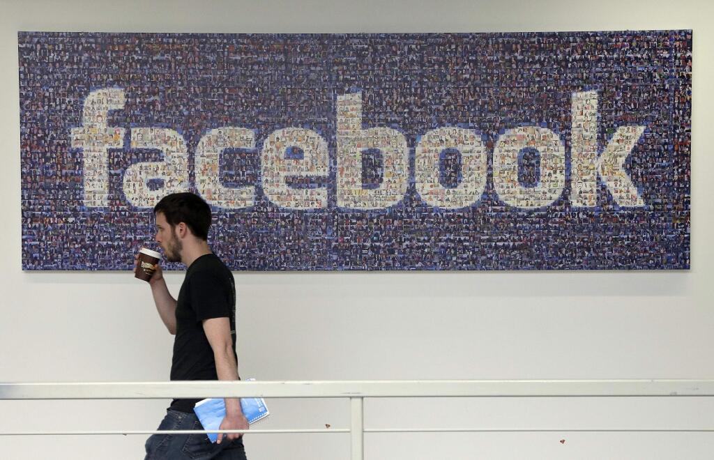 FILE - In this March 15, 2013, file photo, a Facebook employee walks past a sign at Facebook headquarters in Menlo Park, Calif. The San Jose Mercury News reports Saturday, March 17, 2018 that building permits compiled by Buildzoom show Facebook plans to erect the 465,000 square-foot (43,200 square-meter) building at its campus in Menlo Park, Calif. (AP Photo/Jeff Chiu, File)