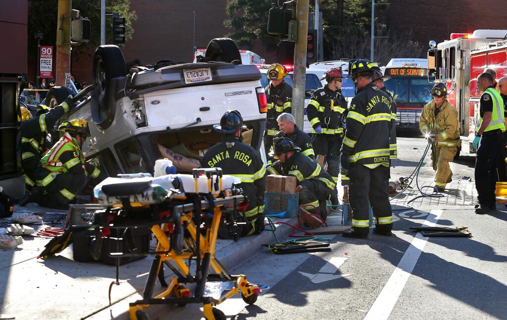 Santa Rosa firefighters work to free a pedestrian from under an overturned vehicle at Third and B streets, in Santa Rosa on Tuesday, Jan. 20, 2015. The pedestrian died on scene. (CHRISTOPHER CHUNG/ PD)