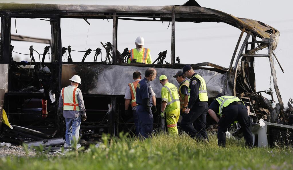 FILE - In this April 11, 2014, file photo, officials and California Highway Patrol Officers look over the remains of a tour bus that was struck by a FedEx truck on Interstate 5 in Orland, Calif. More than a year after the fiery wreck between a FedEx semi-truck and a charter bus killed 10, including five high school students, authorities are expected to address the biggest remaining question: What caused the crash? On Friday, May 22, 2015, the California Highway Patrol is set to release the results of its 13-month investigation into the Thursday, April 10, 2014 head-on collision in Orland, about 100 miles north of Sacramento. (AP Photo/Jeff Chiu, File)