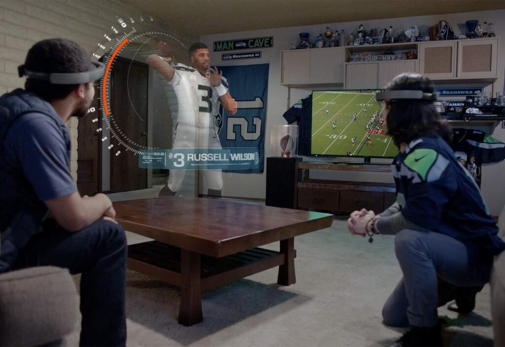A digitally generated recreation of Russell Wilson appears in a room where two users of the Microsoft prototype 'HoloVision' headsets view an enhanced version of a televised football game. (Photo by Microsoft)