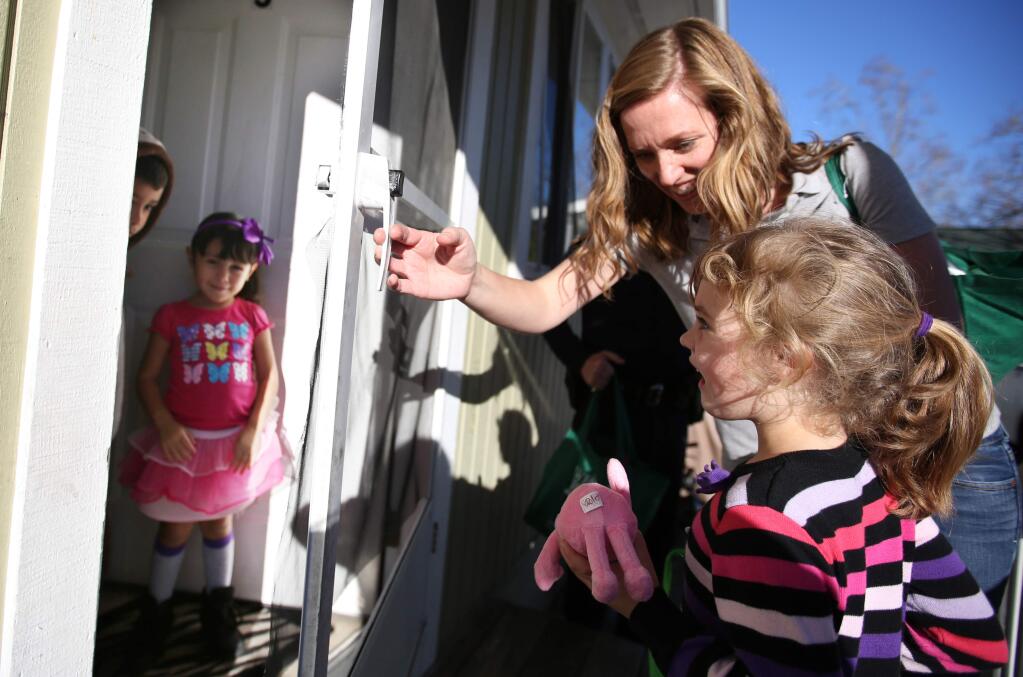 Rebecca Lane, top, helps her daughter Violet Lane-Basler, 5 1/2, open the screen door to hand out candy canes and a stuffed animal to Jaleen Avina, 4, second from left, and her brother Manuel Avina, 7, during a food giveaway as part of a Santa Rosa city neighborhood revitalization program, Monday, December 22, 2014. (Crista Jeremiason / The Press Democrat)