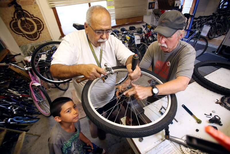 Volunteer Mark Swint, right, helps teach Robert Ramos and his grandson Adrian Murillo fix a wheel from their bicycle at Community Bikes off of Sebastopol Road in Santa Rosa on Thursday, July 25, 2013. (Conner Jay / The Press Democrat)