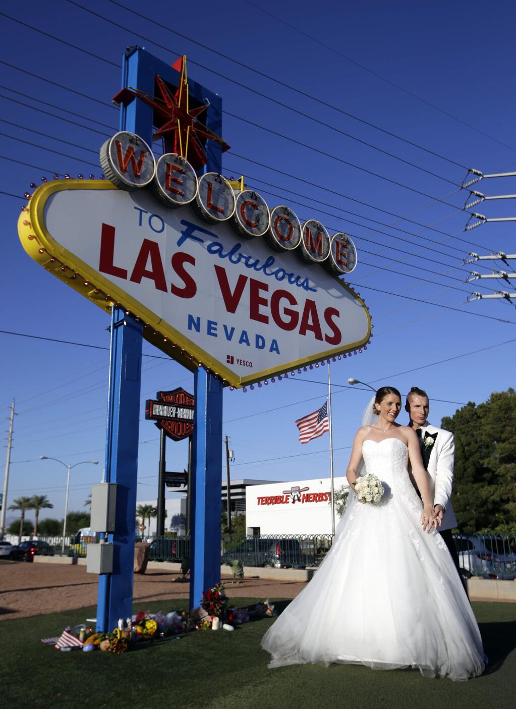 In this Tuesday, Oct. 3, 2017 photo, newlyweds Ann and Sergei Reinchen of Germany, pose for photos in front of the Welcome to Las Vegas sign that has flowers honoring the people who died in a mass shooting on Sunday in Las Vegas. But even though the city is in mourning, for many it is business as usual with celebrations and parties continuing. (AP Photo/Chris Carlson)