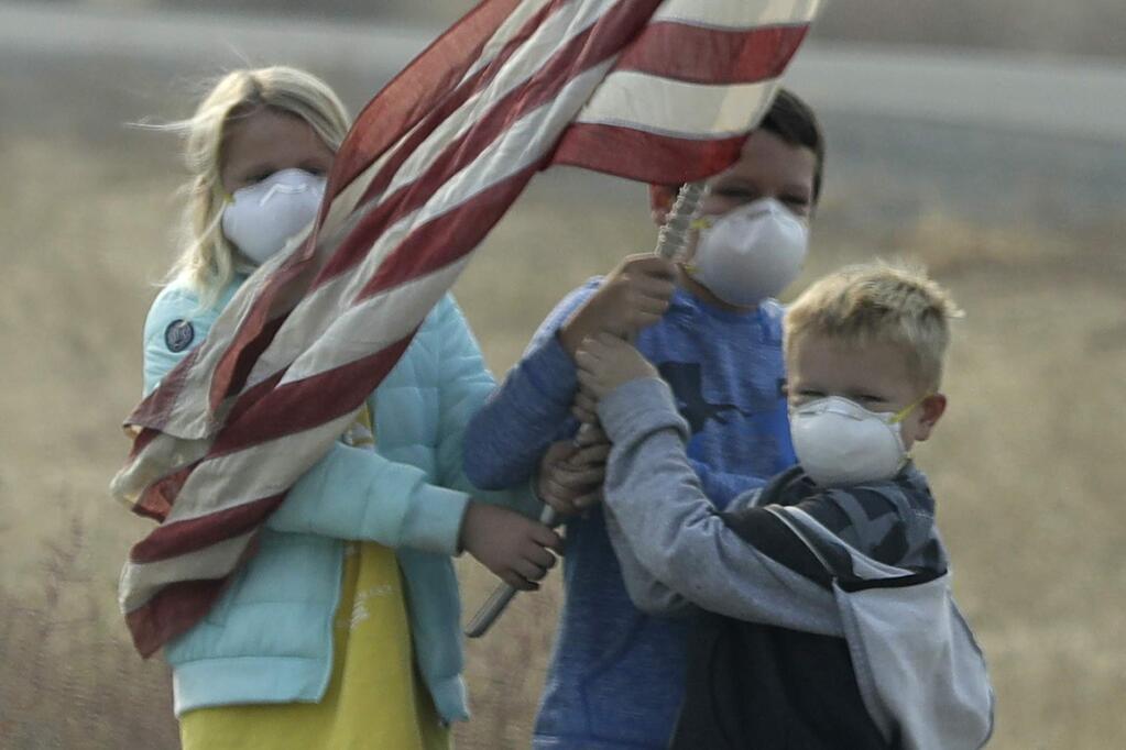 Children stand on the side of the road holding an American flag as the motorcade of President Donald Trump drives through Chico, Calif., on a visit to areas affected by the wildfires, Saturday, Nov. 17, 2018. (AP Photo/Evan Vucci)