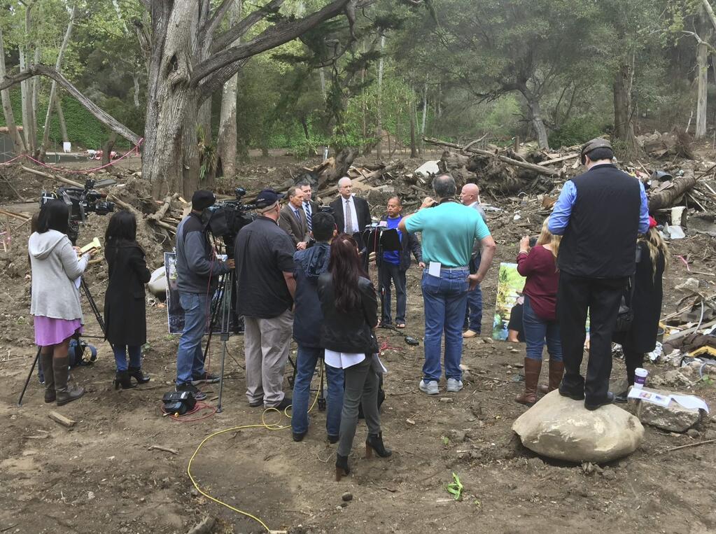 In this photo provided by G.F.Bunting survivor and co-plaintiff Lalo Barajas, center, whose partner Peter Fleurat was killed during devastating debris flows in January at their home, speaks at the site in Montecito, Calif, Thursday, March 29, 2018. Attorneys from left, Joseph Liebman, Geoff Spreter, Peter Bezerk, and Alex Robertson, right, announced the filing of a wrongful-death lawsuit by Barajas and Fleurat's siblings claiming Southern California Edison transformers ignited California's largest-ever wildfire in December. The suit says the blaze could have been prevented and the debris flows wouldn't have happened as a result. (Russ Stanton/G.F.Bunting via AP)