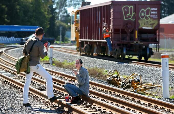 Sage Fiflield, left, and Christine Canady talk along the railroad tracks, near the end of 4th Street, as a freight car carrying gravel rolls by, in Santa Rosa on Wednesday, February 25, 2015. (Christopher Chung/ The Press Democrat)