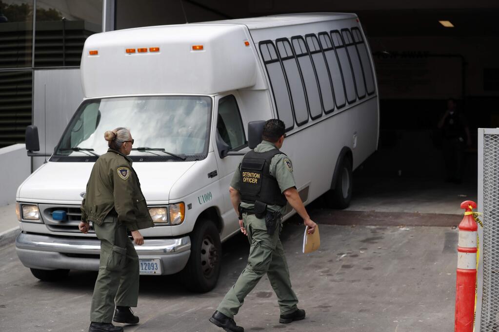 FILE - In this Tuesday, March 19, 2019 file photo, a van carrying asylum seekers from the border is escorted by security personnel as it arrives at immigration court, in San Diego. A federal appeals court ruled Tuesday, May 7, 2019, that the Trump administration can force asylum seekers to wait in Mexico for immigration court hearings while the policy is challenged in court, handing the president a major victory, even if it proves temporary. (AP Photo/Gregory Bull, File)