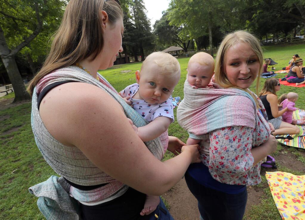 Bethany Seldon, with Ronan, 6 months, helps Victoria and Alice, 5 months, Salisbury adjust her woven wrap at the Big Latch On event at Howarth Park in Santa Rosa. (JOHN BURGESS / The Press Democrat)