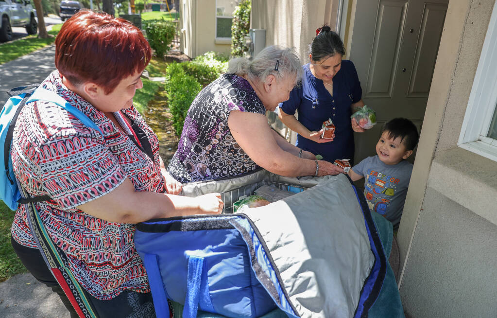 Volunteers Dalia Villagomez, left, and her mother, Estela Pulido, hand out unclaimed summer lunch program meals to Alba Olascoaga and Emiliano Vasquez, 3, at Cypress Ridge, a Burbank Housing Community, in Santa Rosa, Tuesday, July 18, 2023.  (Christopher Chung / The Press Democrat)