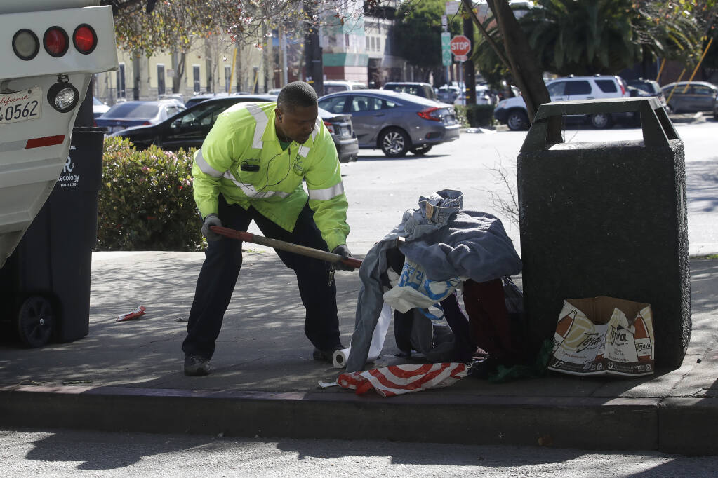 A Recology San Francisco worker picks up clothing and bags next to a trash can in San Francisco, Tuesday, Feb. 18, 2020. (AP Photo/Jeff Chiu)