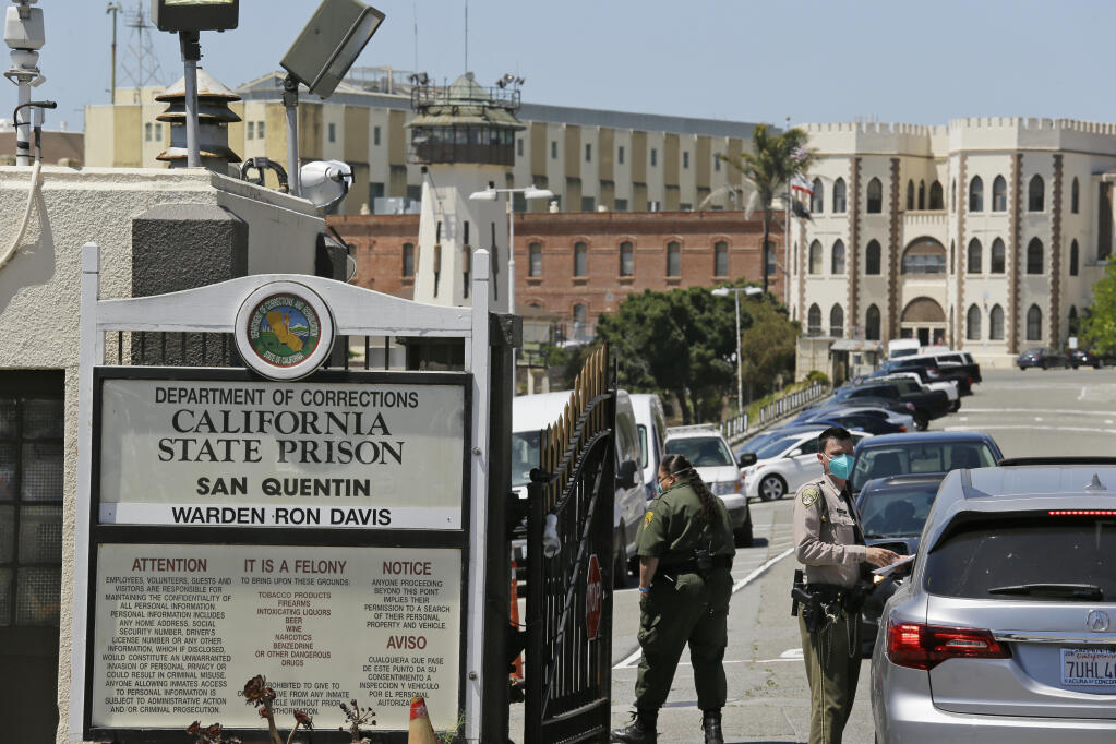 FILE - In this July 9, 2020 file photo a correctional officer checks a car entering the main gate of San Quentin State Prison, in San Quentin, Calif. (AP Photo/Eric Risberg,File)