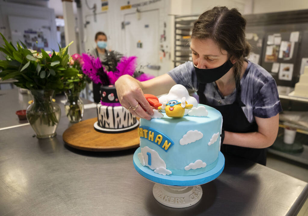 Gergana Karabelov, co-owner of Patisserie Angelica, puts the finishes touches on birthday cakes for a 1-year-old, right, and a 50-year-old before working on the four wedding/elopement cakes order for this weekend. Orders for wedding cakes have increased in preparation for end of the tier system on June 15 and she is already booked for 7 wedding cakes, her maximum, on June 23rd.  (Photo by John Burgess/The Press Democrat)
