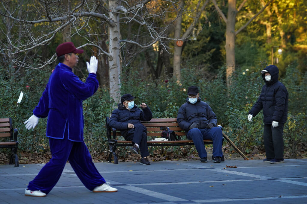 People wearing face masks to help curb the spread of the coronavirus chat each other as a man performs morning exercise at a park in Beijing, Monday, Nov. 23, 2020. (AP Photo/Andy Wong)