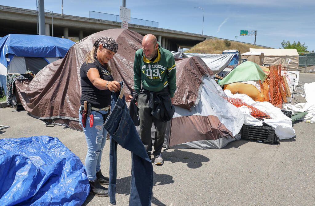 Volunteer Sherrie Vaughn, left, gives a new pair of jeans to homeless encampment resident Donny Vaughn at the city-sanctioned encampment along Roberts Lake Road in Rohnert Park on Monday, May 16, 2022.  (Christopher Chung/ The Press Democrat)