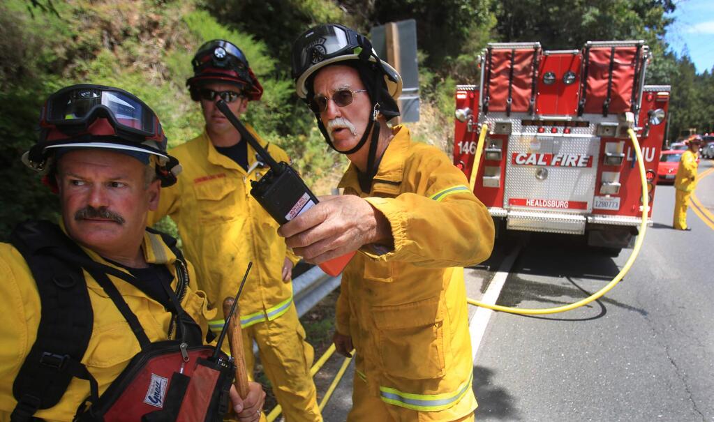 Fire Chief Steve Baxman, 46-year volunteer with Monte Rio Fire, talks with Cal Fire Battalion Chief Mark Gradek, left, and Cal Fire captain Chris Rickert as they discuss which engines to release from a vegetation fire along Highway 116 in Monte Rio, Friday July 15, 2016. (Kent Porter / Press Democrat) 2016